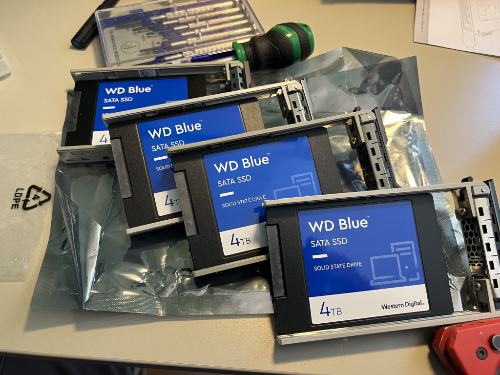 The photo shows 4 x 4TB WD BLUE SATA SSDs sitting in drives cages on a desk. Some tools sit around them.